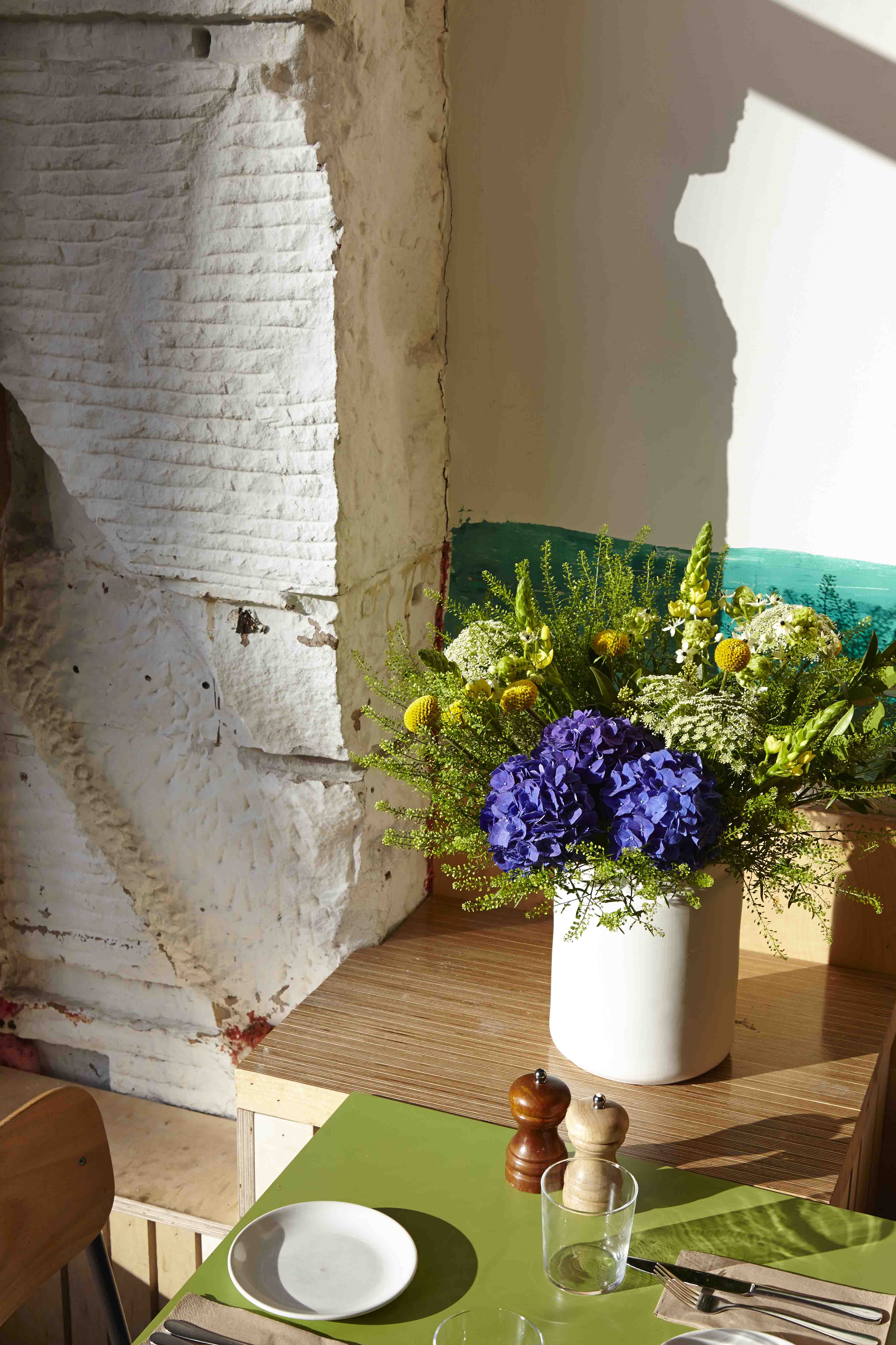 Wooden shelf with flowers in white vase in sunlight.
