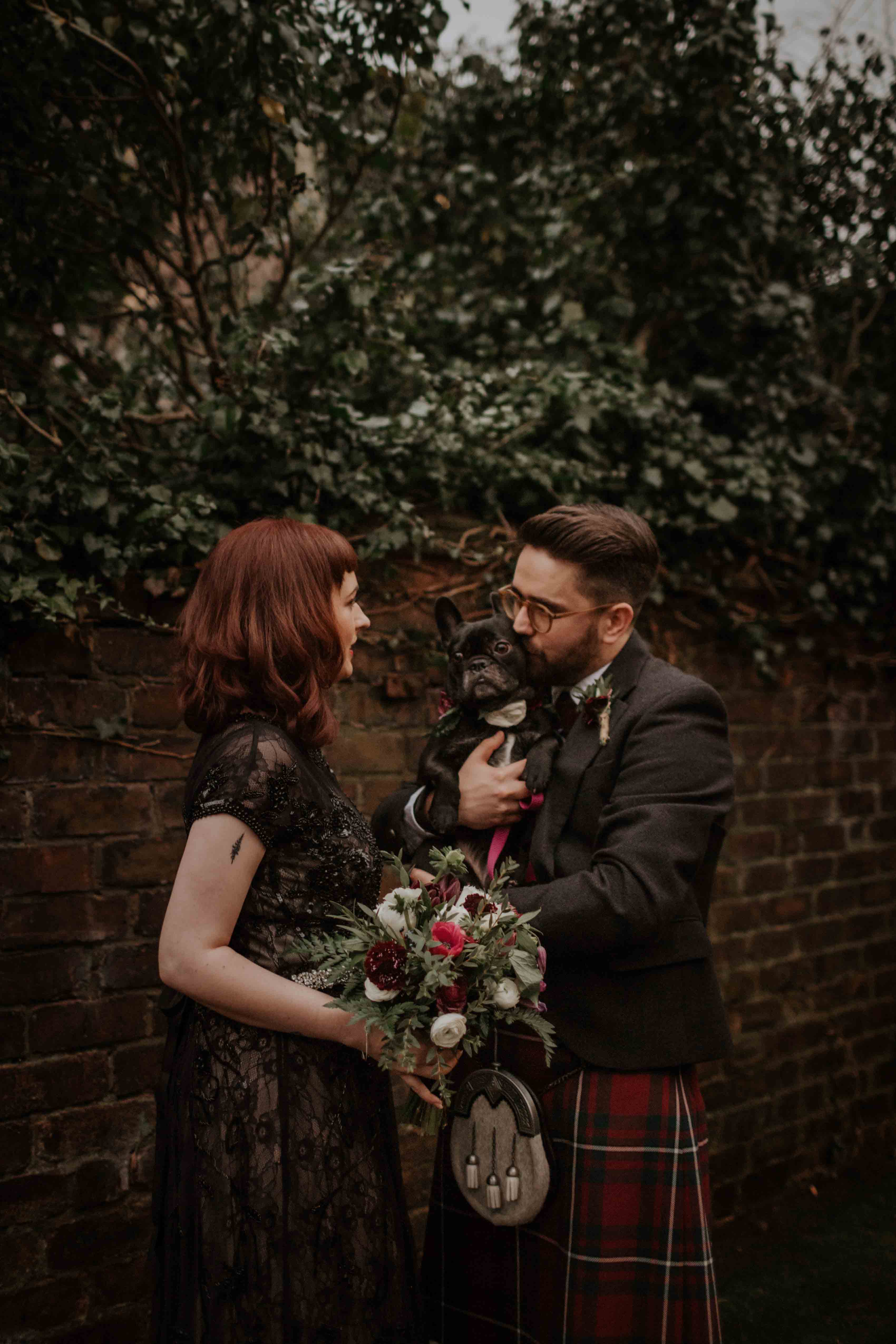 Bride with bouquet. bearded groom wearing glasses and kilt with french bulldog.