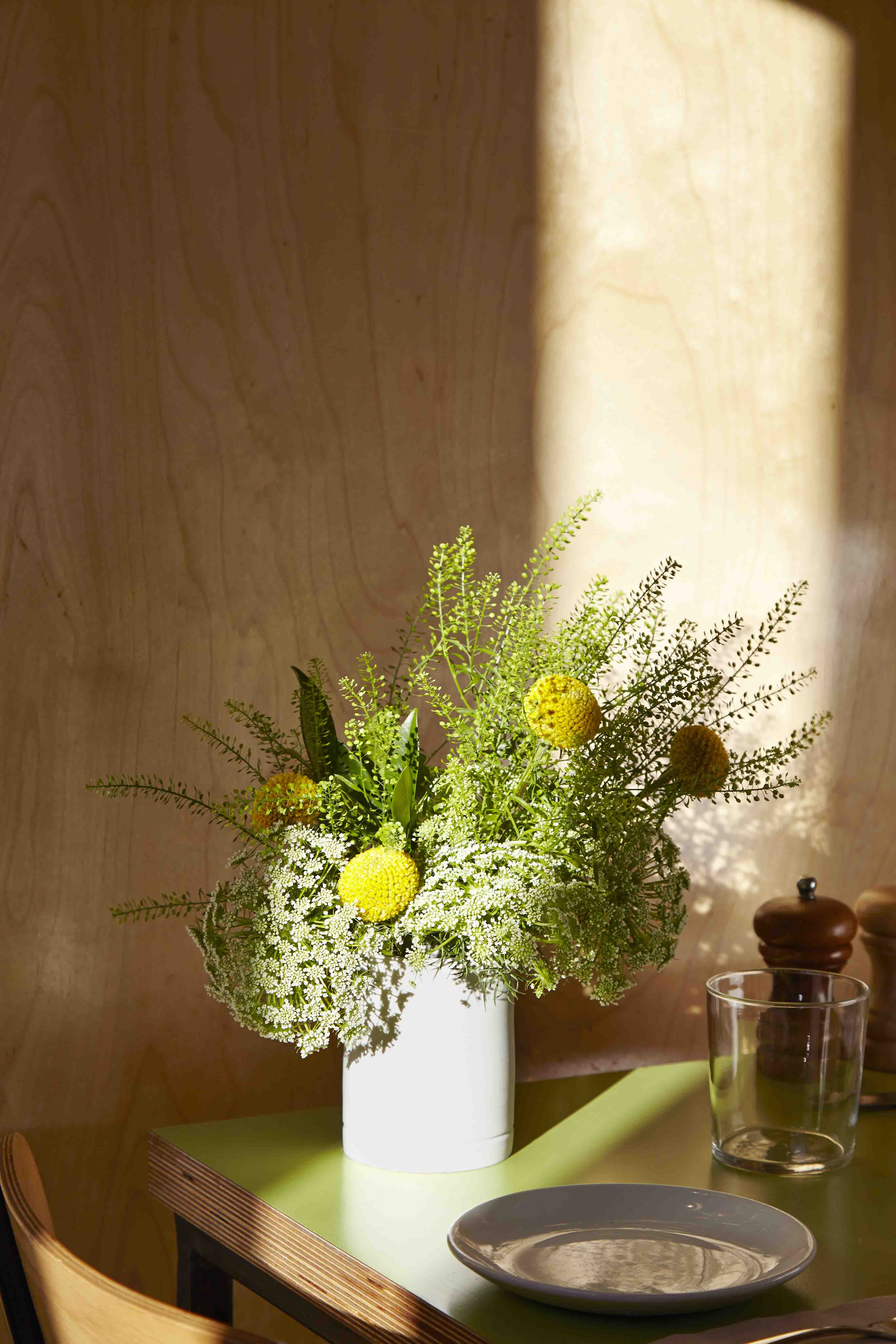 Wooden shelf with flowers in white vase on green table.