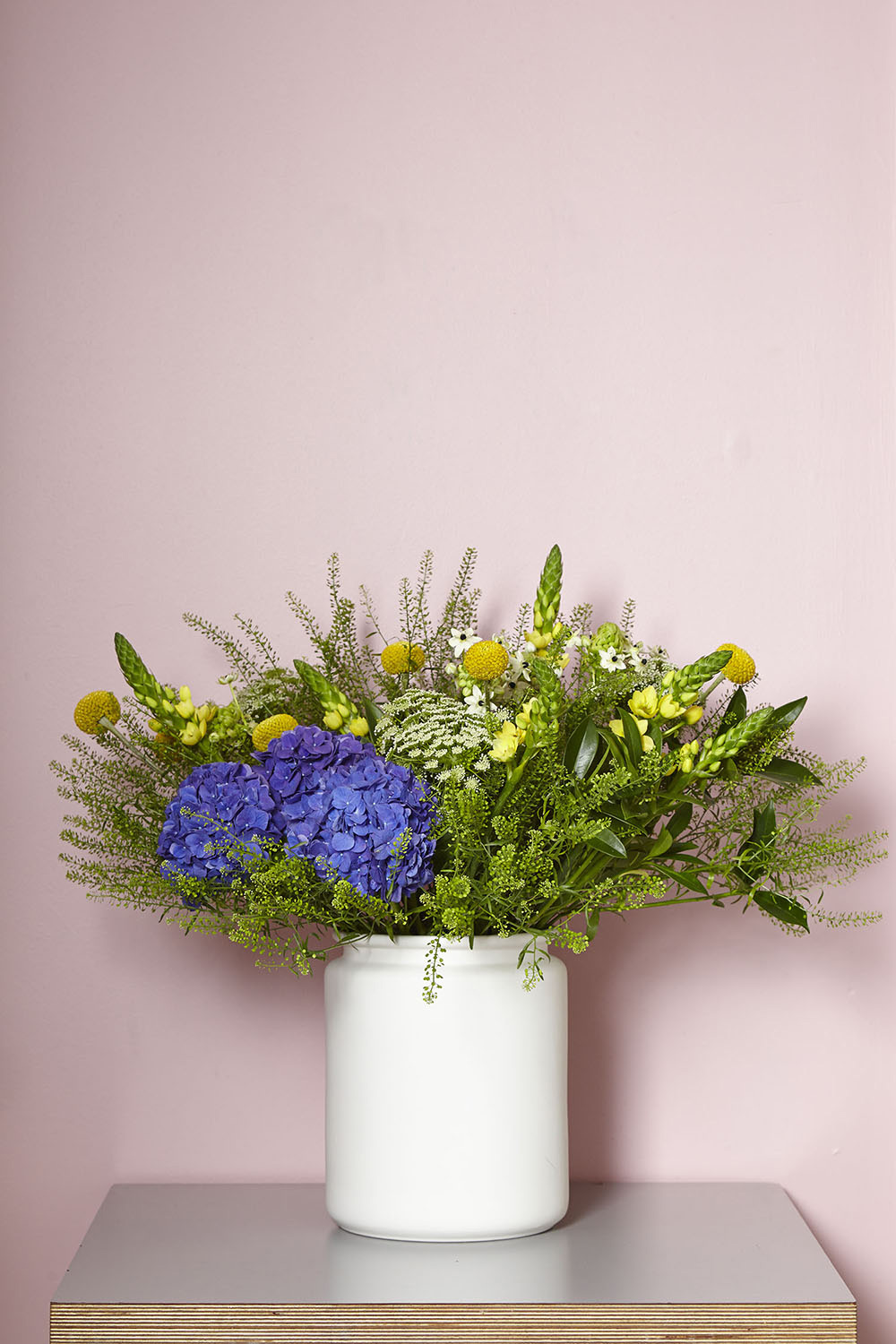 Flowers in vase on grey table with pink wall.