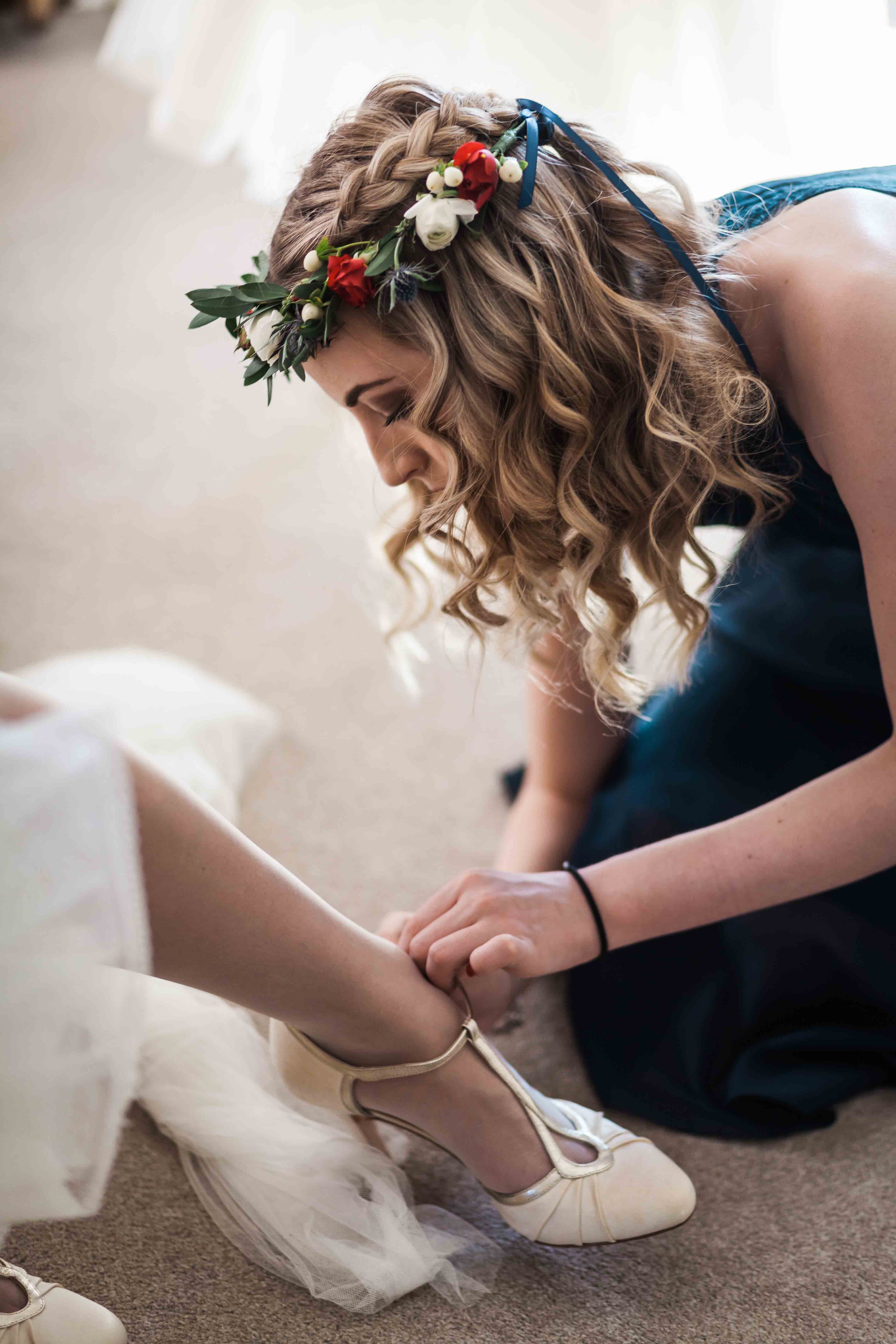 Bridesmaid with flower crown fixing brides shoe. 